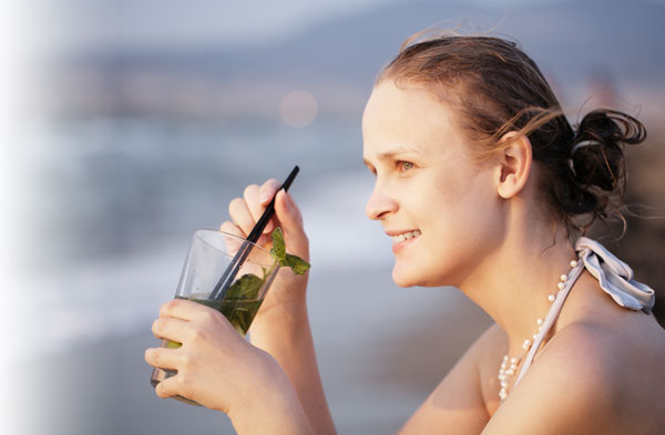 Woman drinking out of class on beach and smiling